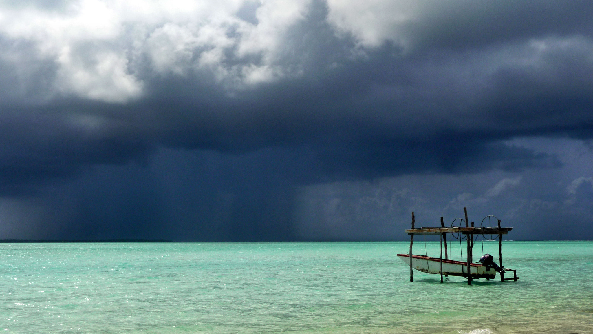 Un bateau sur son support dans le lagon de Maupiti, sous un ciel chargé.